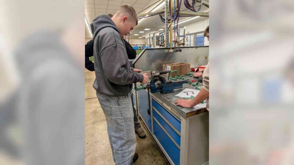 Jugendlicher arbeitet an einer Werkbank mit einer Maschine zur Metallbearbeitung in einer Ausbildungsumgebung.