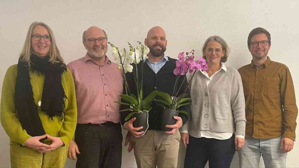 Gruppe von fünf Personen, die zusammen mit Orchideen in Töpfen posieren.