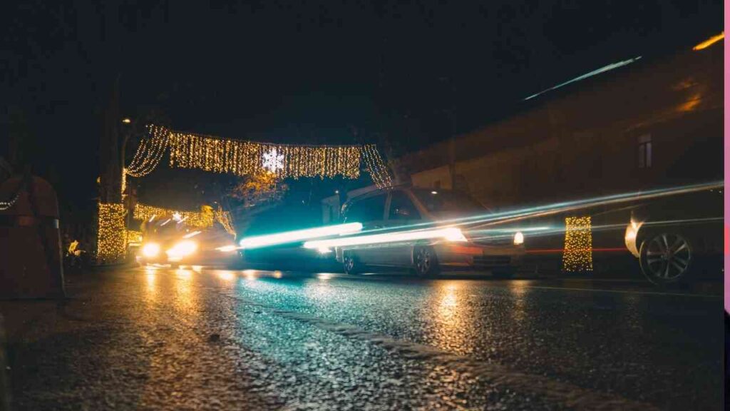 Autos fahren unter einer festlichen Beleuchtung mit Lichtern und Dekorationen auf einer Straße bei Nacht.