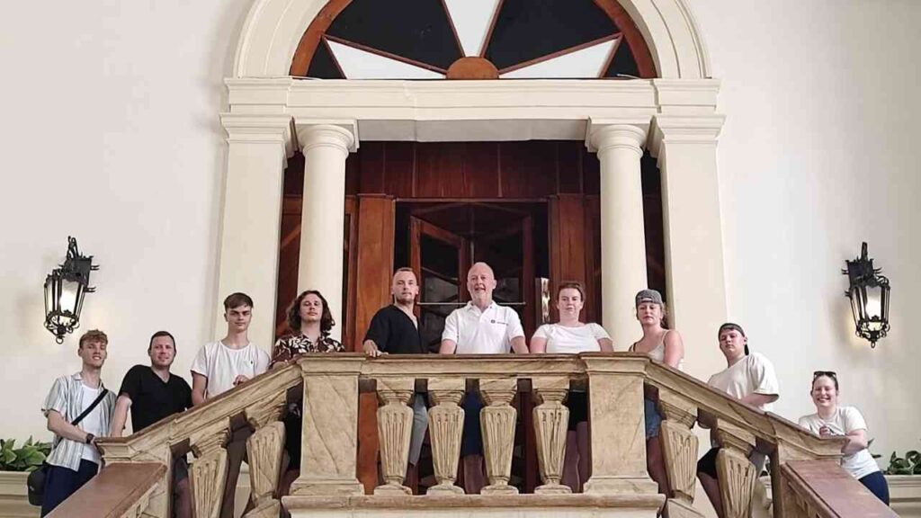 Gruppe von Menschen, die auf einer Treppe in einem Gebäude posieren, mit Säulen und einer großen Tür im Hintergrund.