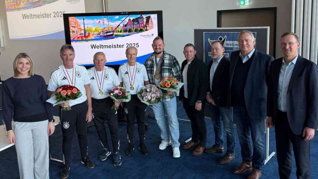 Gruppe von Personen mit Medaillen und Blumenarrangements bei einer Veranstaltung zur Ehrung der Weltmeister 2025.