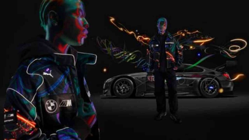 Person in einer bunten Jacke von Puma und BMW, neben einem Rennwagen auf schwarzem Hintergrund.