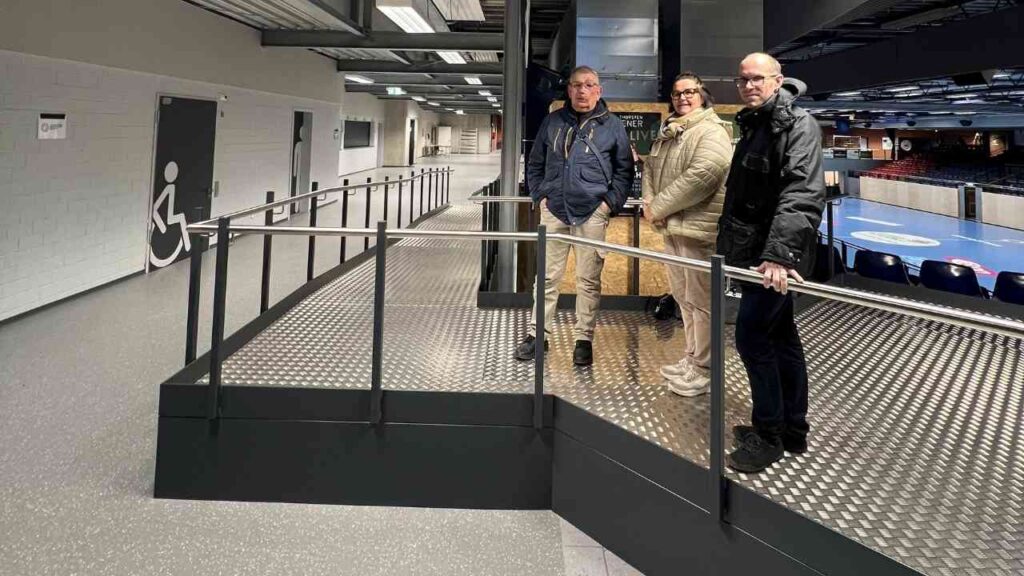 Rollstuhlpodest mit Rampen und drei Personen in einem Innenraum, der Barrierefreiheit demonstriert.