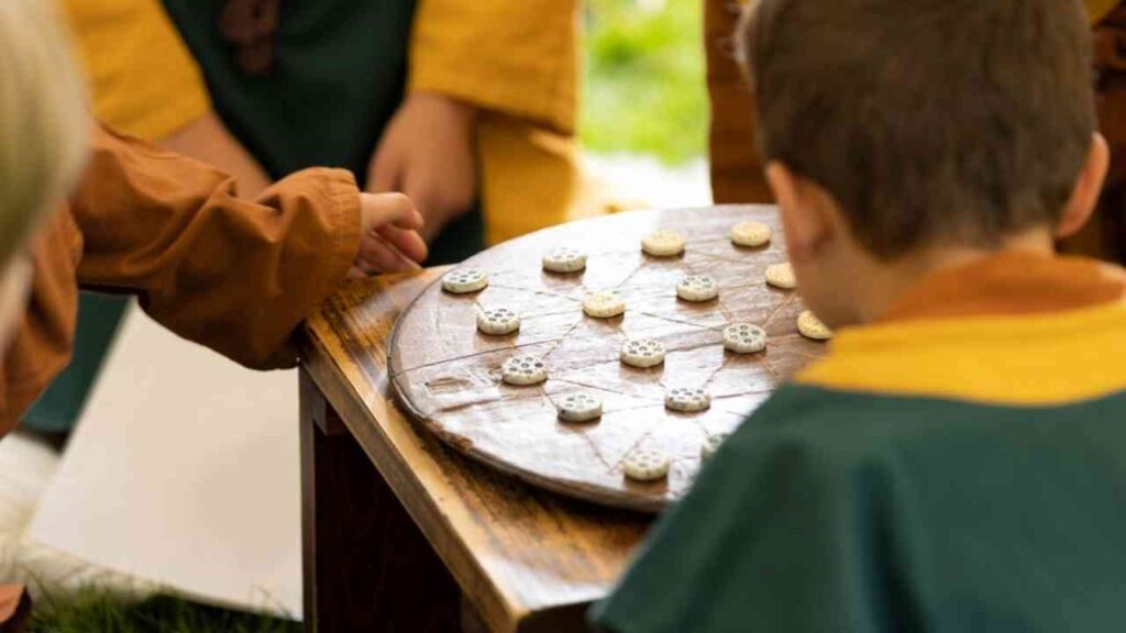 Kinder spielen ein traditionelles Brettspiel mit Holzsteinen auf einem runden Spielbrett im Freien.