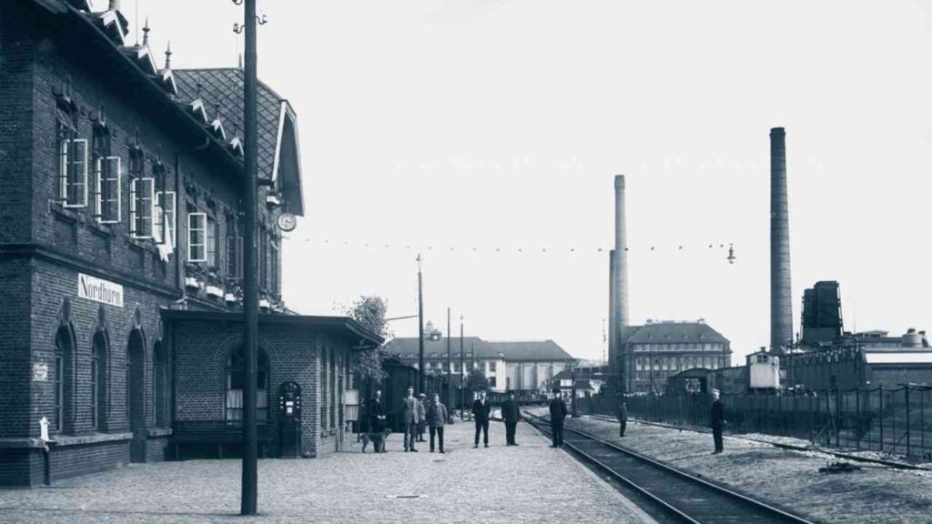 Bahnhofgebäude mit historischen Zügen und Personen auf dem Bahnsteig in Nordhorn.