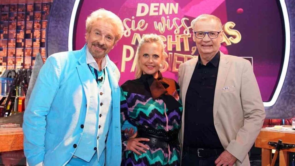 Thomas Gottschalk, Barbara Schöneberger und Günther Jauch posieren vor einem bunten Hintergrund bei einer Fernsehsendung.