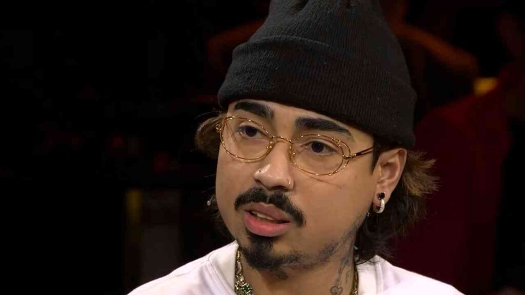 Mann mit Brille und Mütze, der in einem Interview spricht, mit sichtbaren Tattoos im Gesicht.