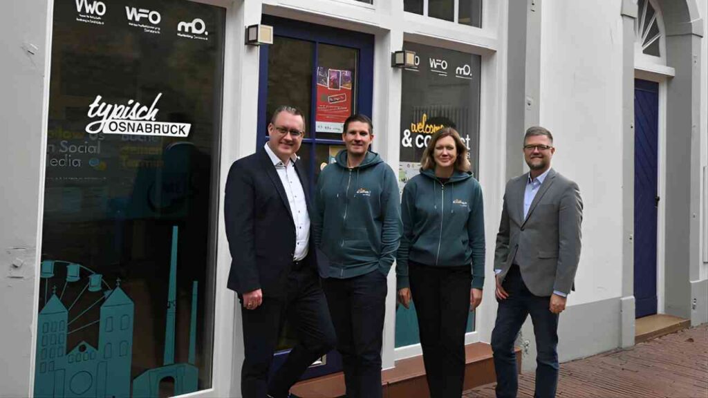 Vier Personen stehen vor einem Geschäft mit Fenstern, die mit Grafiken und Texten gestaltet sind.