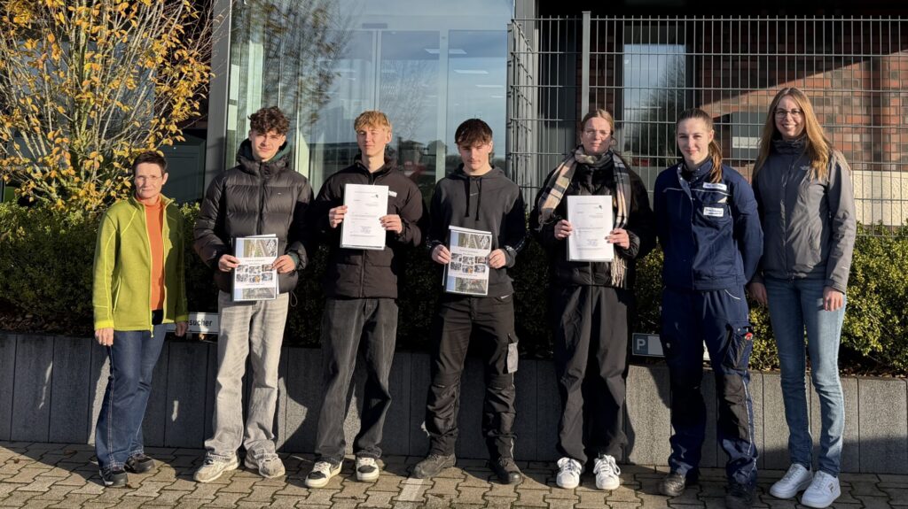 Gruppe von sechs Personen, die Zertifikate in den Händen halten, vor einem Gebäude im Freien.