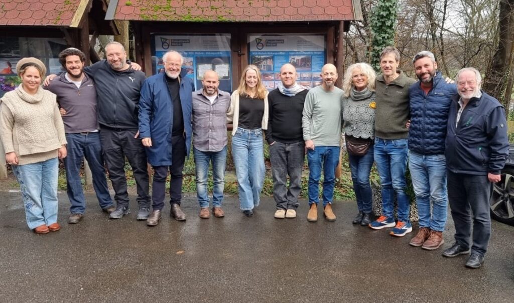 Gruppe von Personen, die zusammenstehen, mit verschiedenen Kleidungsstilen und Frisuren, auf einem Gehweg in einem Park.