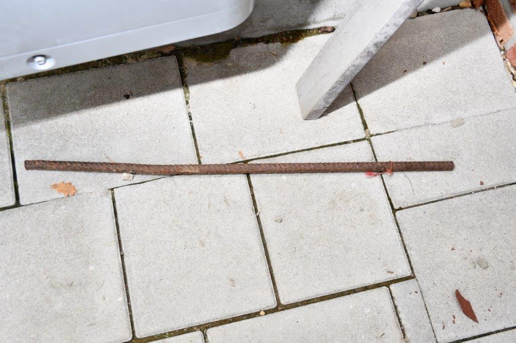 Ein rostiger Eisenstab liegt auf einem gepflasterten Boden in einem Außenbereich.