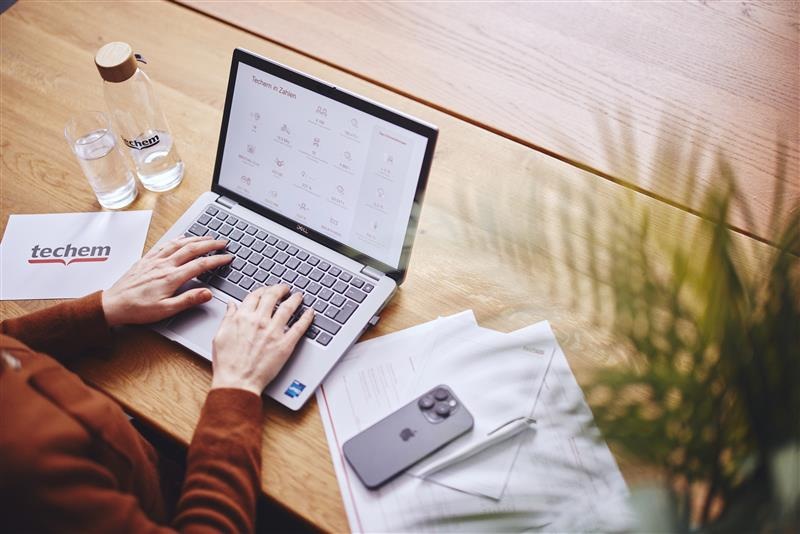 Person, die auf einem Laptop mit einer Benutzeroberfläche von Techem arbeitet, während sie auf einem Holztisch sitzt.