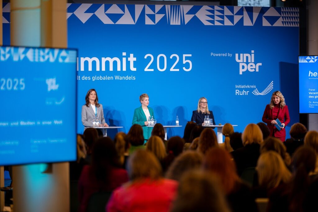 Vier Frauen auf einer Bühne während des Her Summit 2025 mit einem blauen Hintergrund und dem Schriftzug 'Her Summit 2025'.