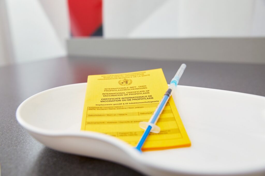 Gelbes Impfheft mit Spritze auf einem weißen Teller, bereit zur Verwendung in einer medizinischen Umgebung.