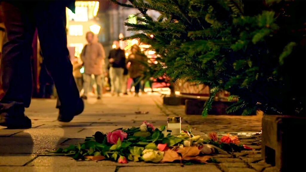 Bunte Blumen und Kerzen auf dem Boden eines Weihnachtsmarktes in Magdeburg, umgeben von festlicher Beleuchtung.