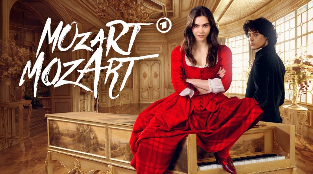 Frau in rotem Kleid sitzt auf einem Klavier mit dem Schriftzug 'Mozart' im Hintergrund.