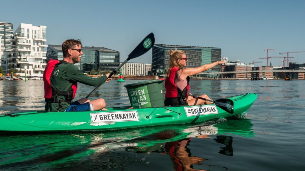 Zwei Personen paddeln in einem grünen Kajak auf ruhigem Wasser in Kopenhagen.