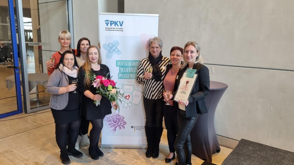 Gruppe von Frauen, die bei einer Veranstaltung mit Auszeichnungen und Blumen posieren, vor einem Banner der PKV.