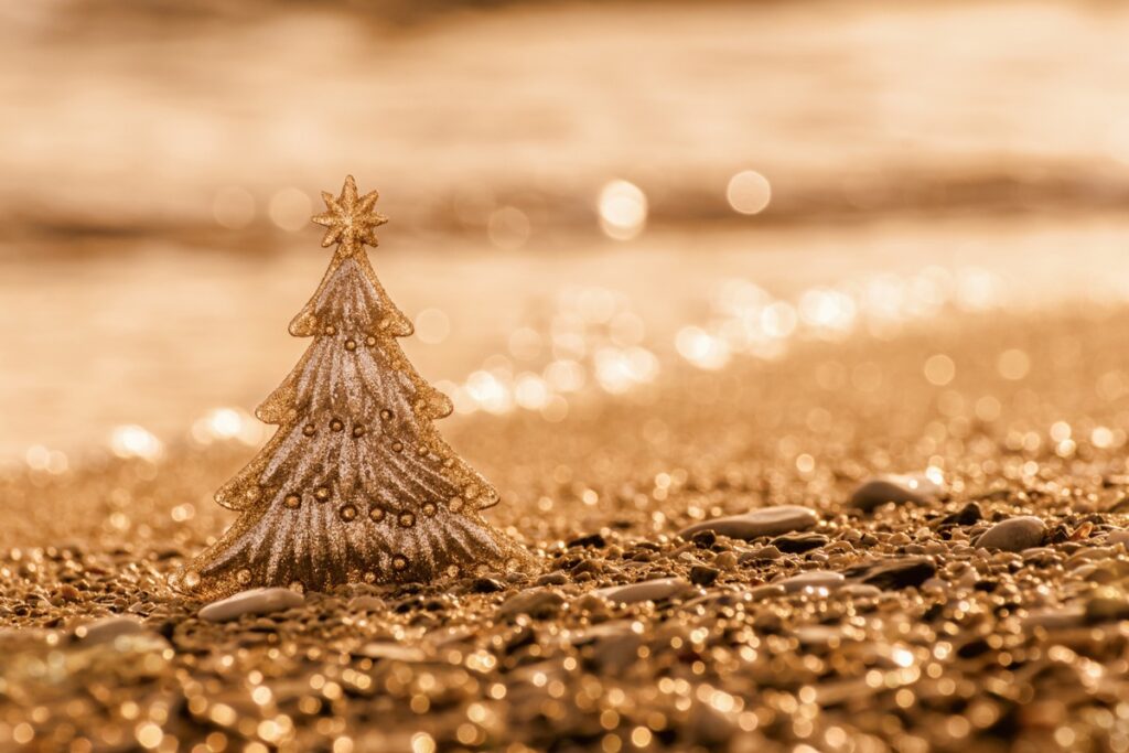 Goldener Weihnachtsbaum aus Dekoration auf einem sandigen Untergrund mit glitzernden Lichtern im Hintergrund.