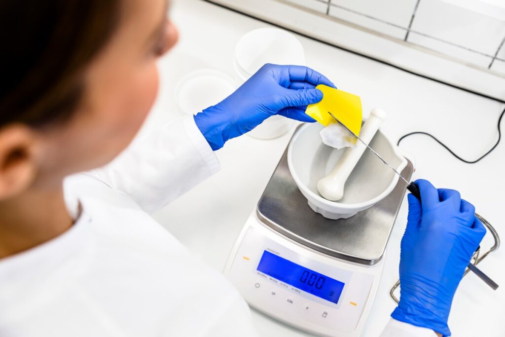 Laborantin wiegt Zutaten mit einer digitalen Waage in einem Mörser für chemische Analysen.