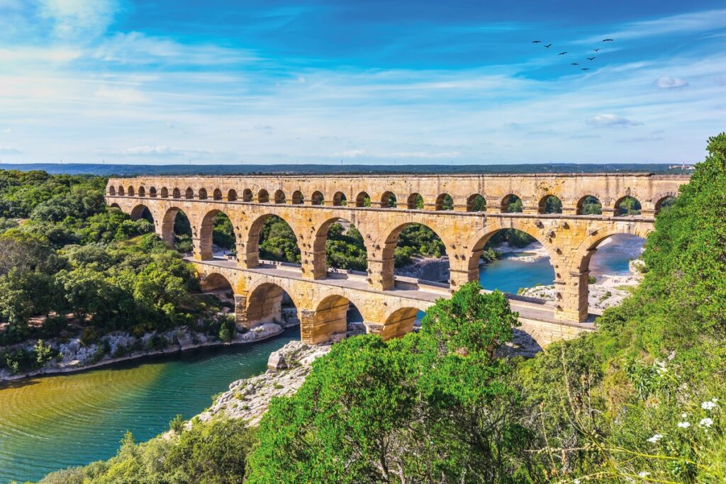 Römisches Aquädukt Pont du Gard mit mehreren Bögen über einem Fluss in einer grünen Umgebung.