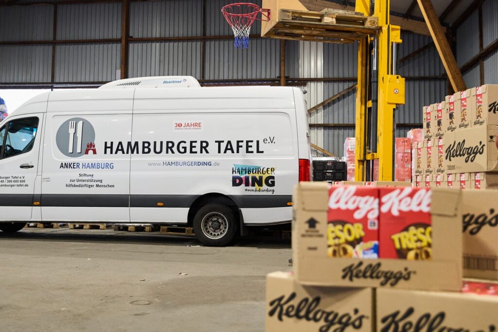 Lieferwagen der Hamburger Tafel e.V. mit Logo und Website auf der Seite, umgeben von Lebensmittelkartons.