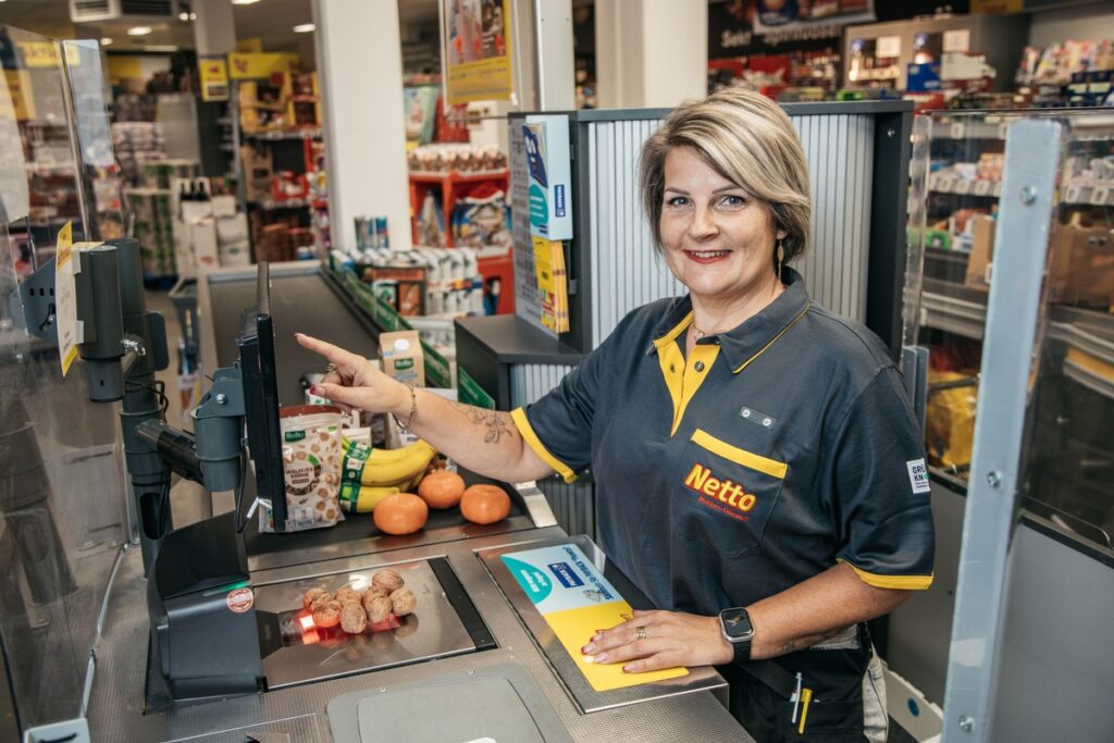 Kassiererin bei Netto, die an einer Selbstbedienungskasse arbeitet und einen Artikel scannt.