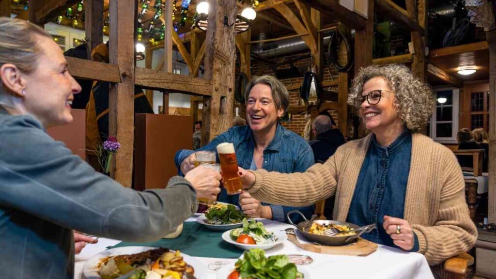 Drei Personen stoßen mit Getränken an, während sie an einem Tisch mit verschiedenen Gerichten sitzen.