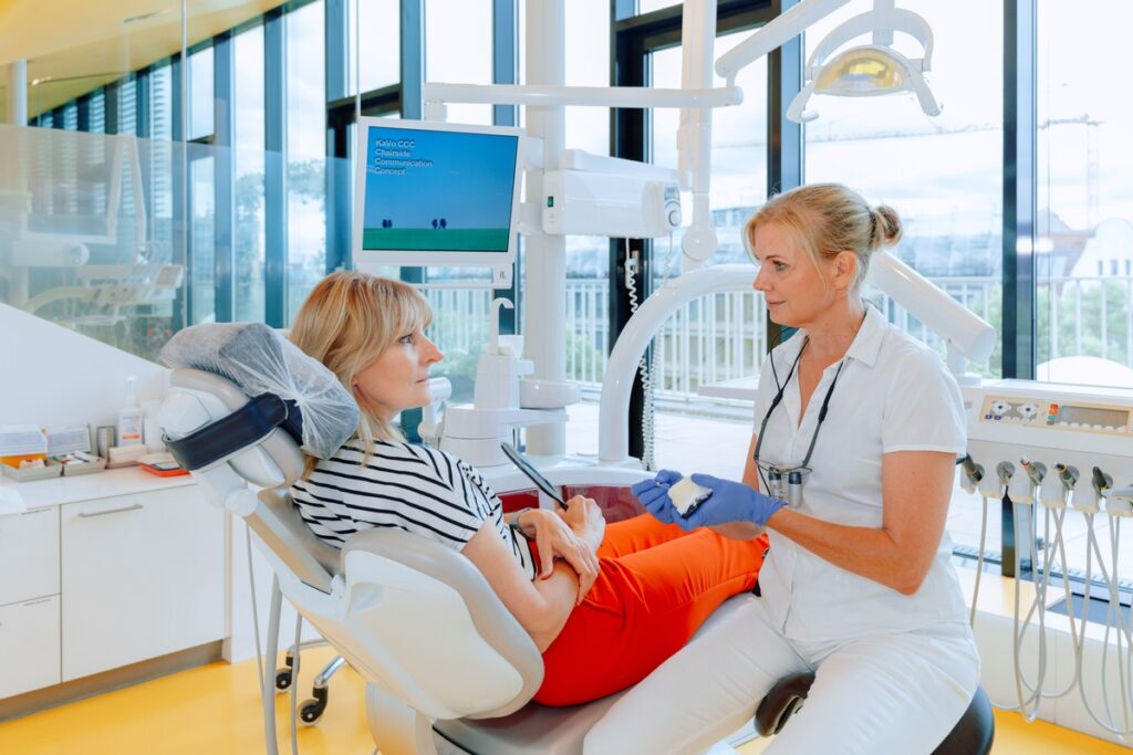 Zahnärztin spricht mit Patientin in moderner Zahnarztpraxis mit Behandlungsstuhl und medizinischer Ausrüstung.