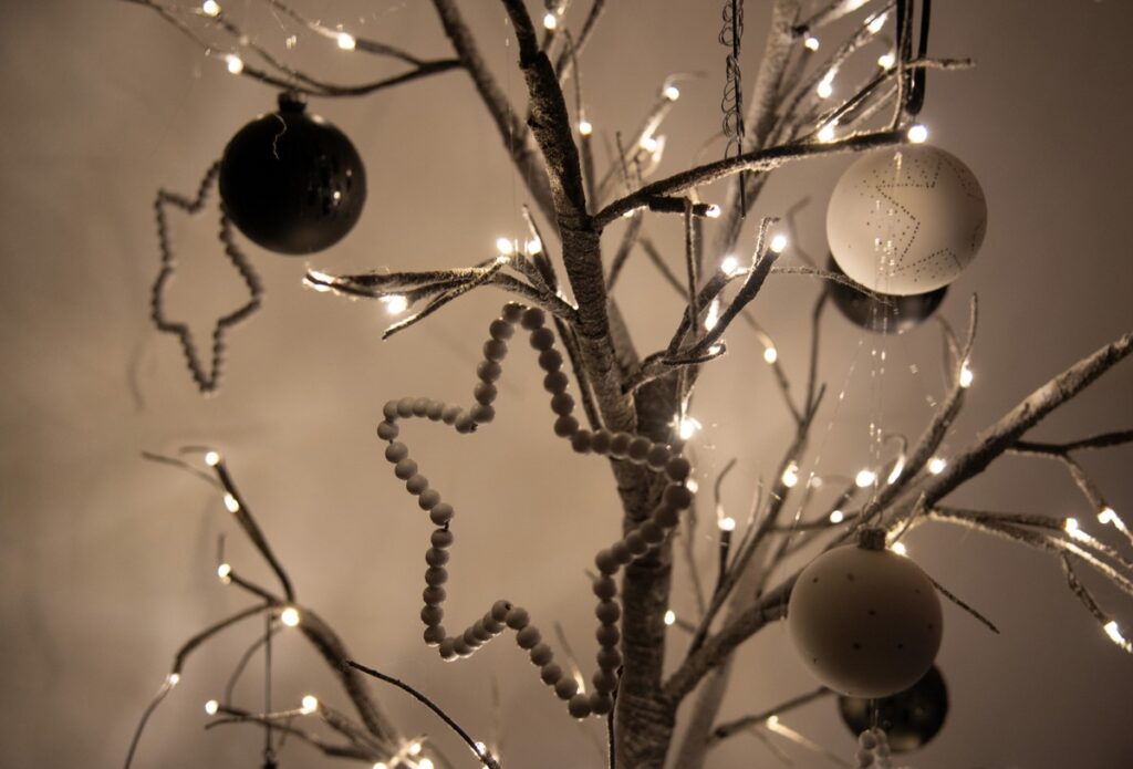 Weihnachtsbaum mit Lichtern und verschiedenen Ornamenten, darunter schwarze und weiße Kugeln sowie Sternanhänger.