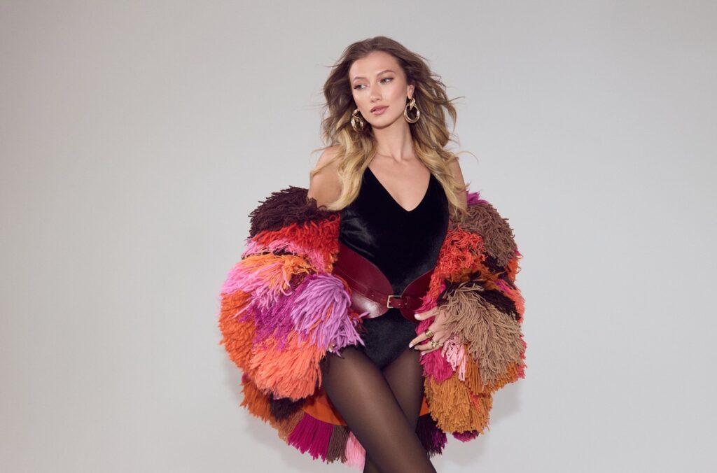 Model trägt einen bunten, flauschigen Mantel mit verschiedenen Farbtönen und einem schwarzen Body.