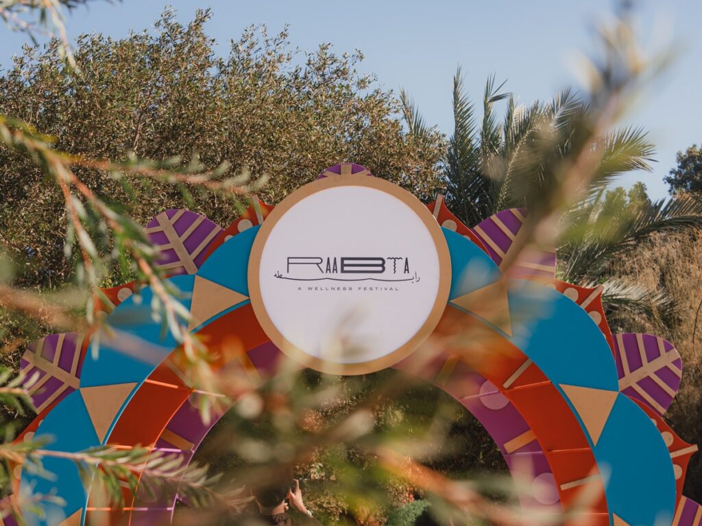 Bunte Bogenstruktur mit dem Logo des Rabta Wellness Festivals, umgeben von Pflanzen und Bäumen.