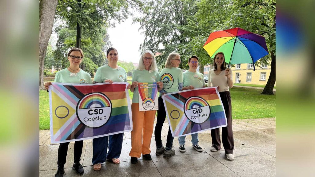 Gruppe des Coesfelder CSD-Orga-Teams mit T-Shirts, Regenbogenflaggen und Plakat
