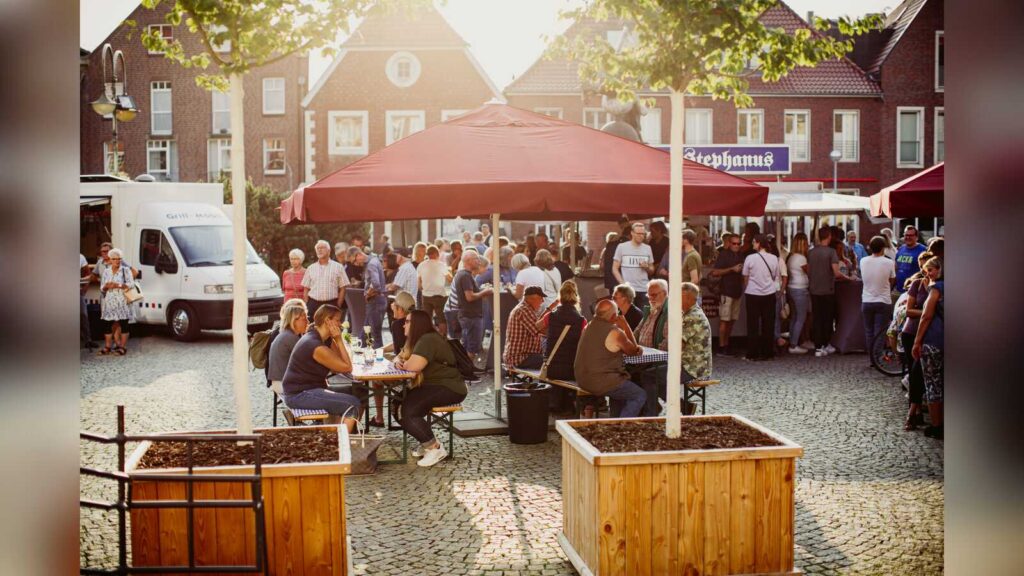 Besetzte Tische auf dem Coesfelder Marktplatz beim Feierabendmarkt im Abendlicht