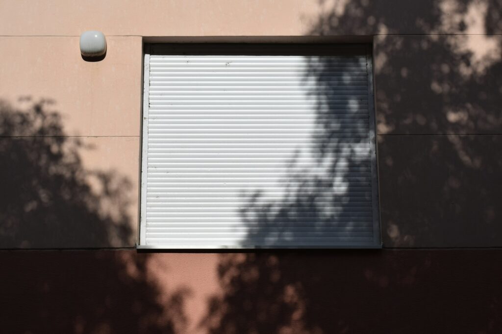 Fenster mit geschlossener Jalousie, davor Schatten von Blaettern