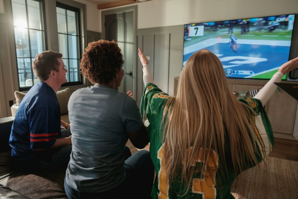 Mehrere Menschen sitzen zusammen vor einem Fernseher und schauen ein Sportspiel