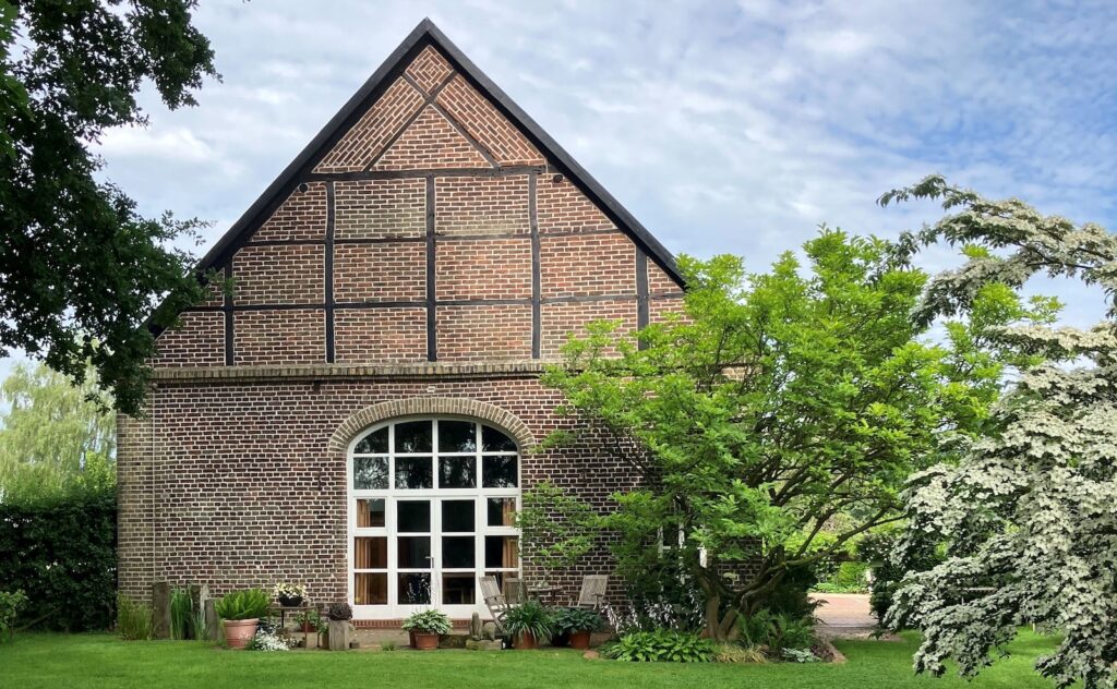Backsteinhaus mit Fachwerkgiebel und großem Rundbogenfenster hinter einem gepflegten Rasen im Garten Christensen in Lüdinghausen