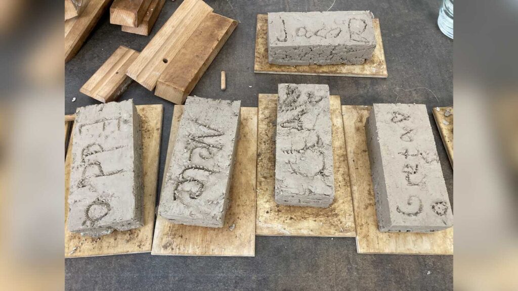 Selbst geformte Ziegelsteine mit eingeritzten Namen liegen auf Holzbrettern
