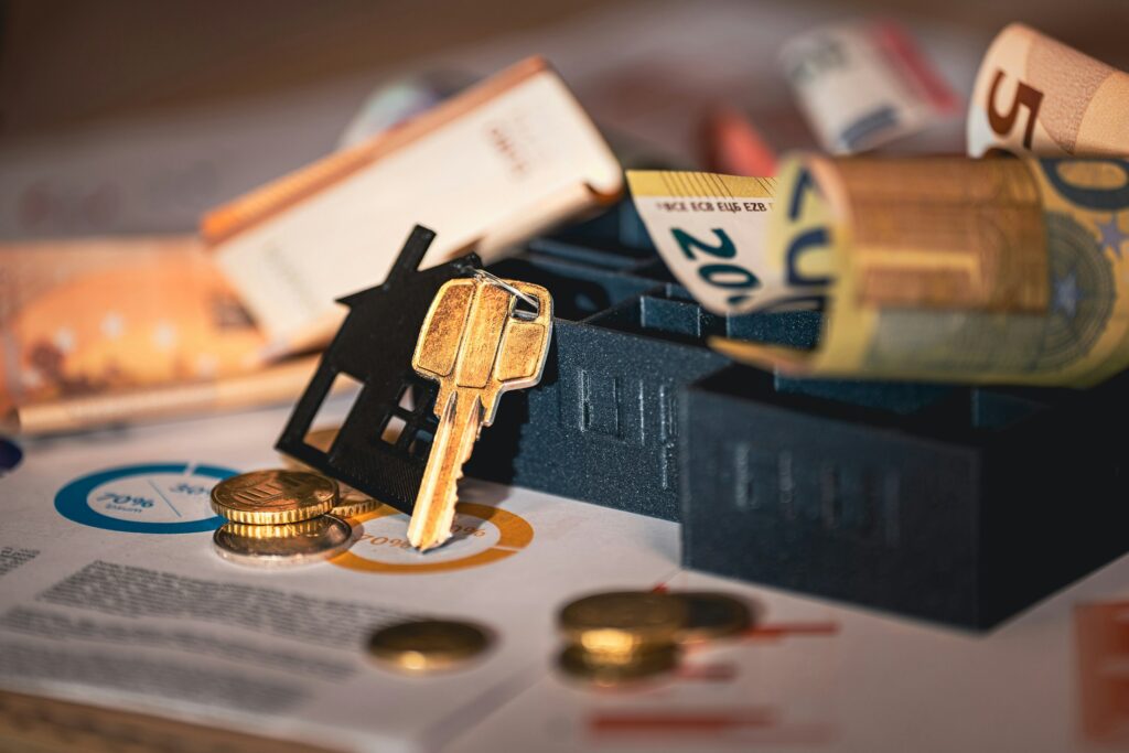 Hausmodell, Schluessel und Unterlagen zu Wohnkosten auf einem Tisch