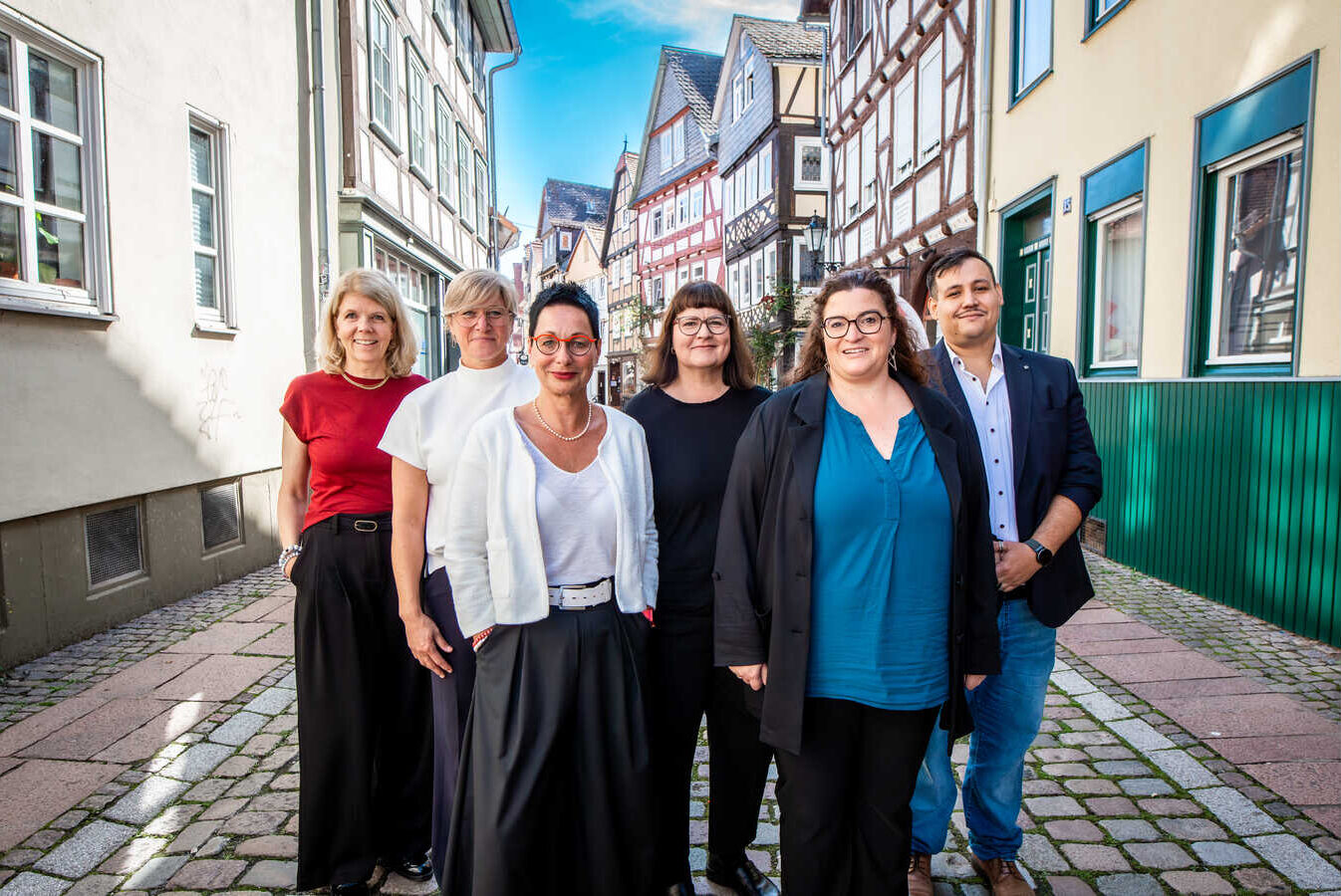 Sechs Menschen stehen in einer Fachwerkgasse und blicken in die Kamera