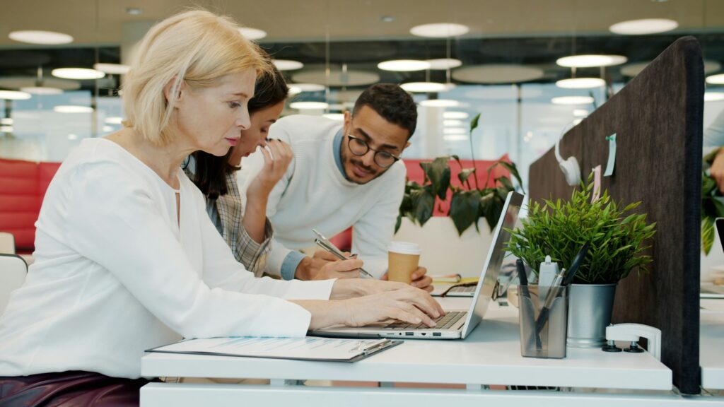 Kolleginnen und Kollegen arbeiten gemeinsam an Laptops in einem Großraumbüro