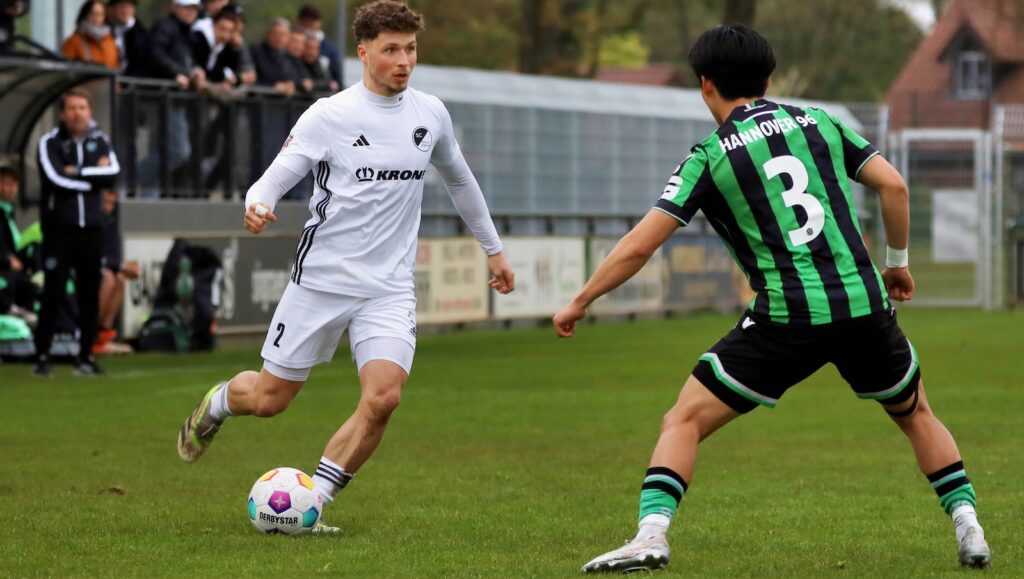 Jonas Tepper im weißen Trikot des SC Spelle-Venhaus im Zweikampf mit einem Spieler von Hannover 96 II