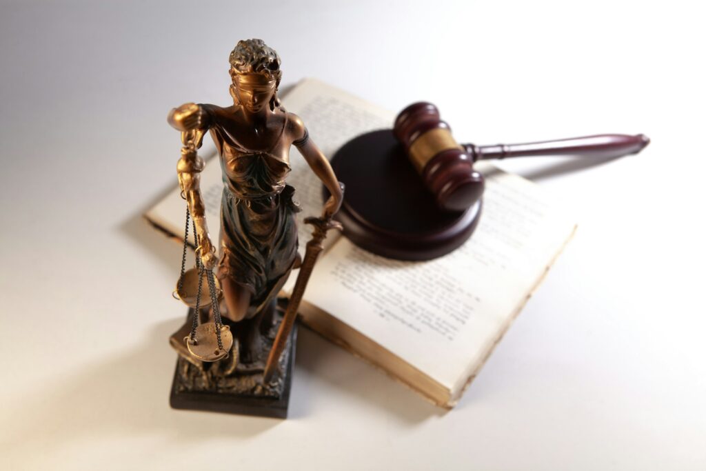 Justitia-Figur, Richterhammer und aufgeschlagene Gesetzbücher auf einem Schreibtisch
