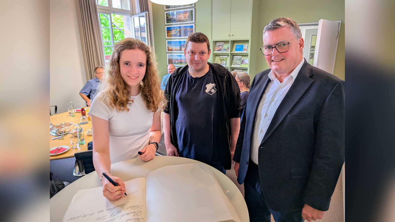 Anna Wilmink trägt sich gemeinsam mit ihrem Trainer Fabian Stotyn und Bürgermeister Thomas Berling ins Goldene Buch der Stadt Nordhorn ein