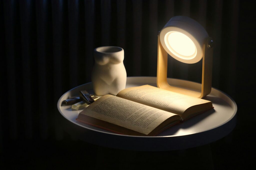 Ein aufgeschlagenes Buch liegt neben einer Lampe auf einem Tisch