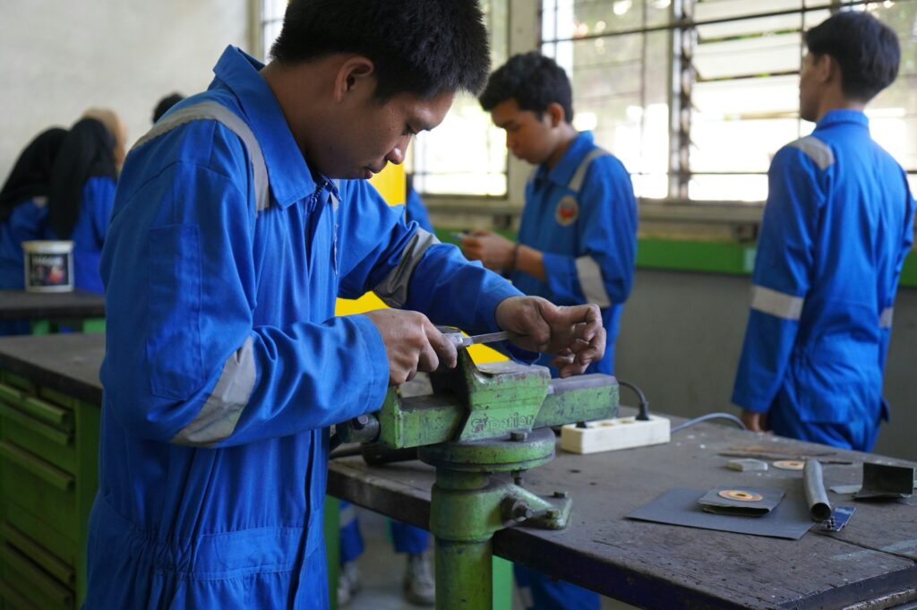 Gruppe junger Menschen arbeitet gemeinsam an einem Metallteil in der Werkstatt, Symbolbild zur Ausbildung im Handwerk