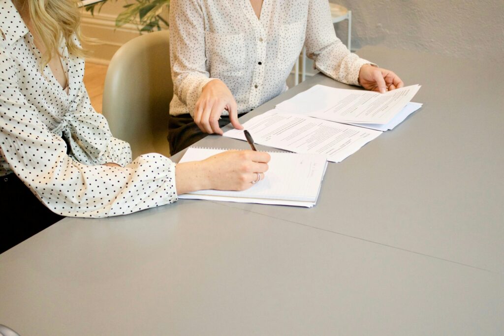 Zwei Frauen am Tisch, eine unterschreibt ein Dokument