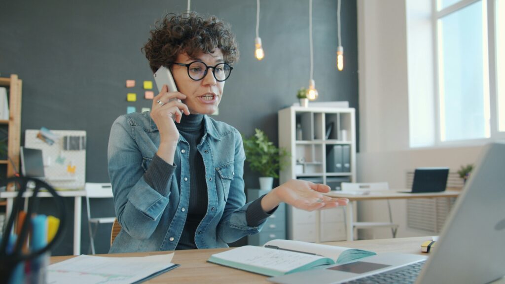 Frau führt ein angespanntes Telefonat im Büro als Symbolbild für einen eskalierenden Konflikt per E-Mail