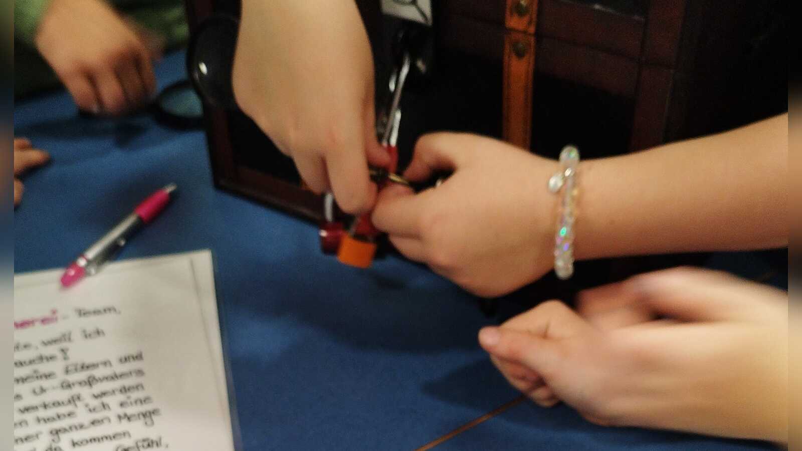 Teilnehmende des SommerLeseClubs lösen beim Escape Game ein Schloss, um die Schatztruhe zu öffnen