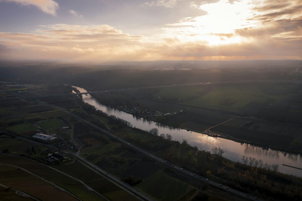 Ein Fluss schlängelt sich unter bewölktem Himmel durch eine grüne, naturnahe Landschaft